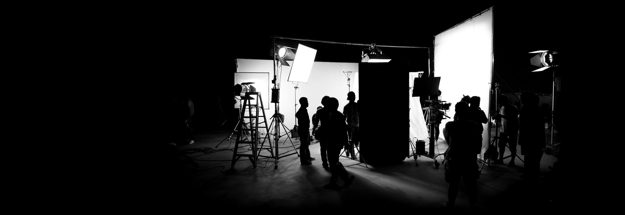Silhouetted Los Films crew and camera on a brightly lit soundstage set